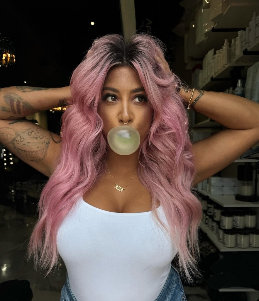 House of Hair client with long bubblegum pink waves blowing a bubble in the salon